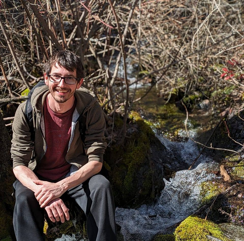 Photo of Matt, sitting in the woods by a stream