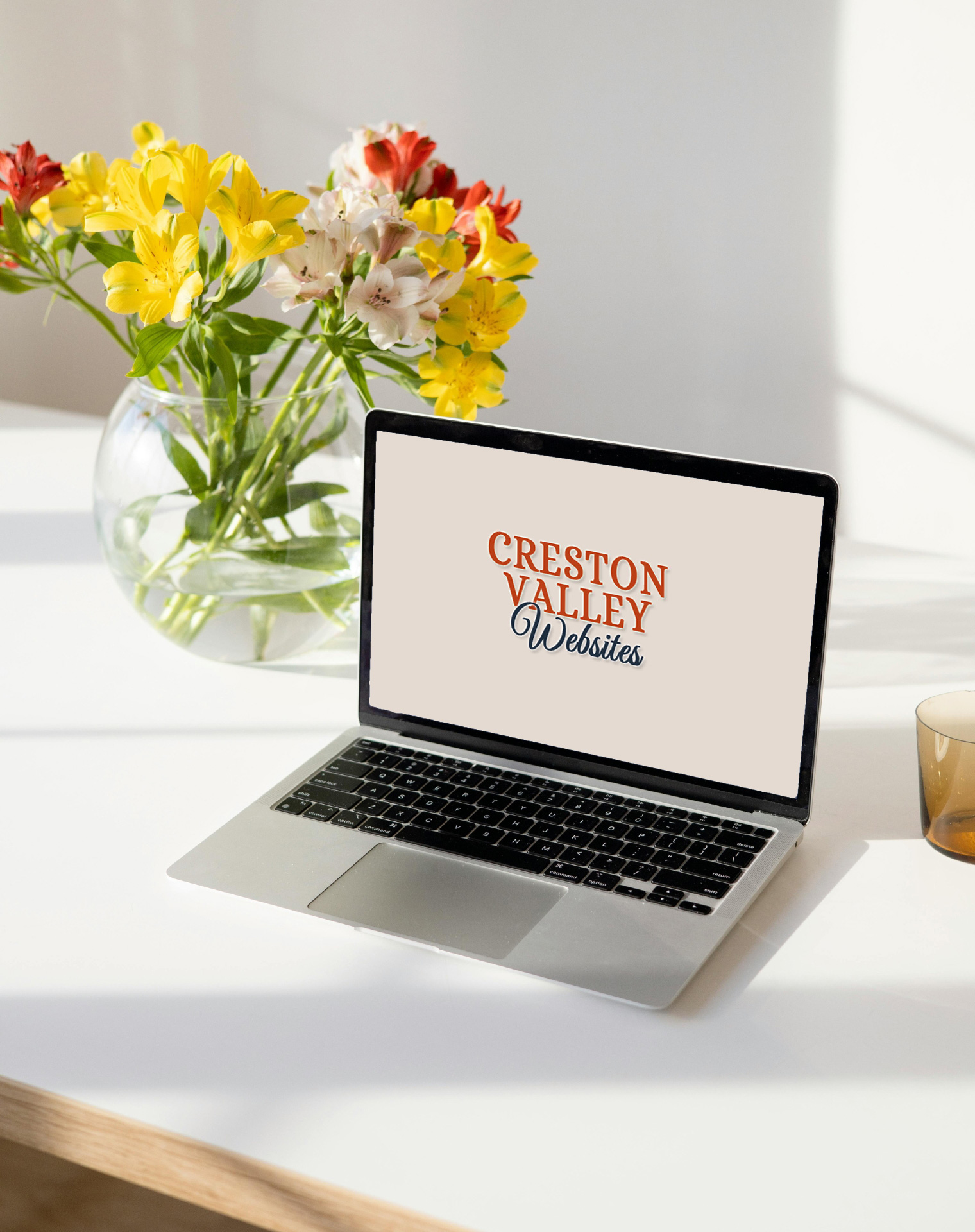 Creston Valley Websites logo on a laptop screen on a table with some flowers in a vase